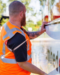 Medewerker van Versluys Verkeerstechniek in oranje veiligheidshesje bevestigt een werkzaamheden-bord langs een waterweg
