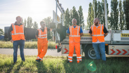 Medewerkers van Versluys Verkeerstechniek staan samen bij een werkvoertuig langs de weg tijdens werkzaamheden in de infrastructuur.
