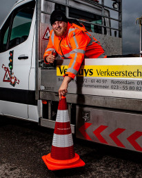 Medewerker van Versluys Verkeerstechniek bij een werkvoertuig met verkeerskegel tijdens uitvoering van verkeersmaatregelen op locatie.