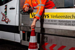 Medewerker van Versluys Verkeerstechniek bij een werkvoertuig met verkeerskegel tijdens uitvoering van verkeersmaatregelen op locatie.