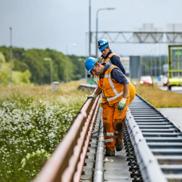 Medewerkers van Versluys Verkeerstechniek werken veilig langs de snelweg met beschermende kleding en verkeersmaatregelen bij wegonderhoud.