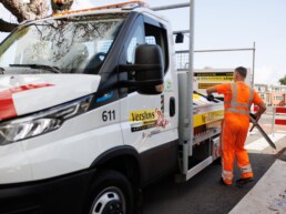 Medewerker van Versluys Verkeerstechniek plaatst tijdelijke verkeersmaatregelen bij een oversteekplaats in stedelijk gebied, naast een 100% elektrische servicewagen