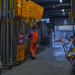 Werfmedewerker in het magazijn van Versluys Verkeerstechniek tussen rekken met verkeersborden en afzetmateriaal