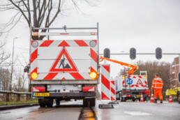 Verkeersmedewerker plaatst tijdelijke verkeersmaatregelen en afzettingen bij werkzaamheden op een natte weg.