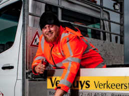 Medewerker van Versluys Verkeerstechniek bij bedrijfswagen met verkeerskegel.