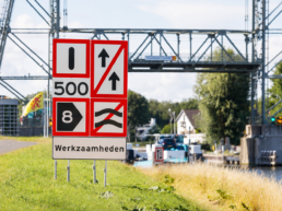 Scheepvaartbord met tijdelijke verkeersmaatregelen bij werkzaamheden langs een vaarweg en brug.